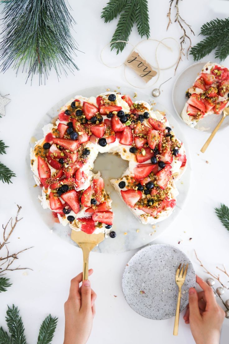 someone is cutting into a cake with strawberries and blueberries on the top, surrounded by pine branches