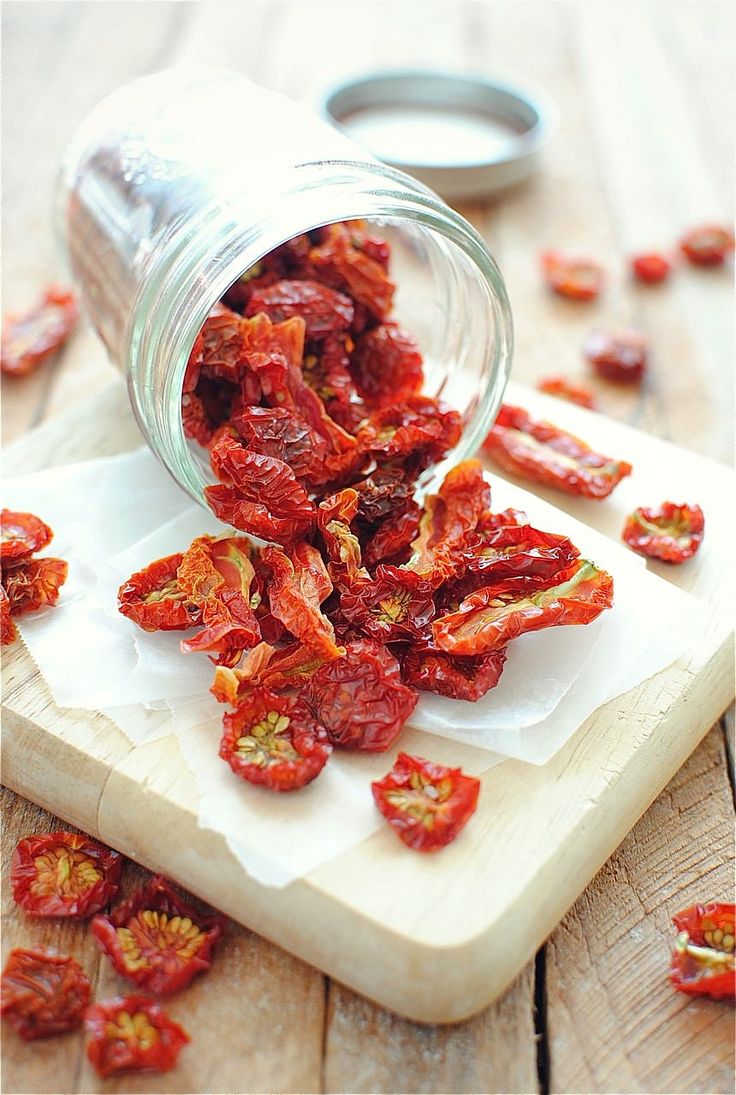 dried goji berries spilling out of a glass jar on a cutting board next to some cut up pieces