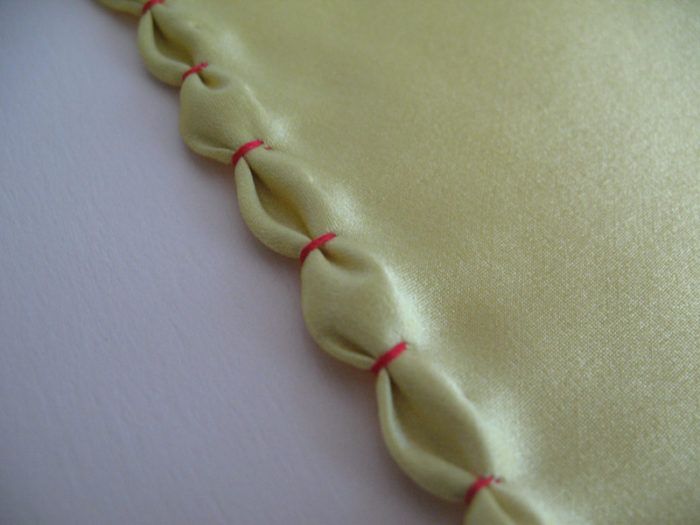 a close up view of a satin fabric with red thread on the edges and an untied knot at the end