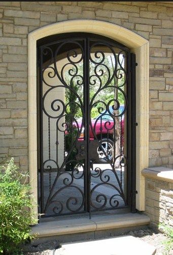 an iron gate is open on the outside of a brick building with a pink car behind it