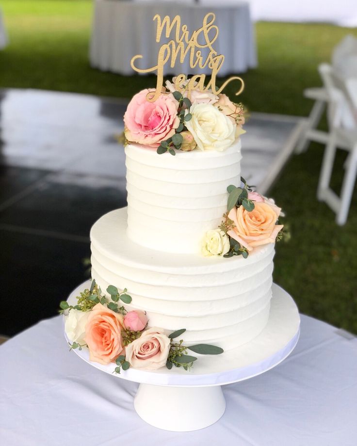 a white wedding cake with flowers and mr and mrs topper on the front tier