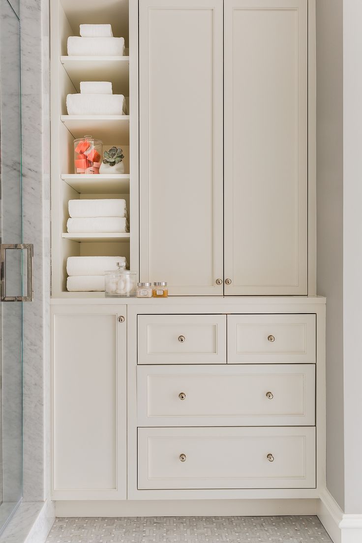 a bathroom with white cabinetry and drawers in the shower area, along with toiletries