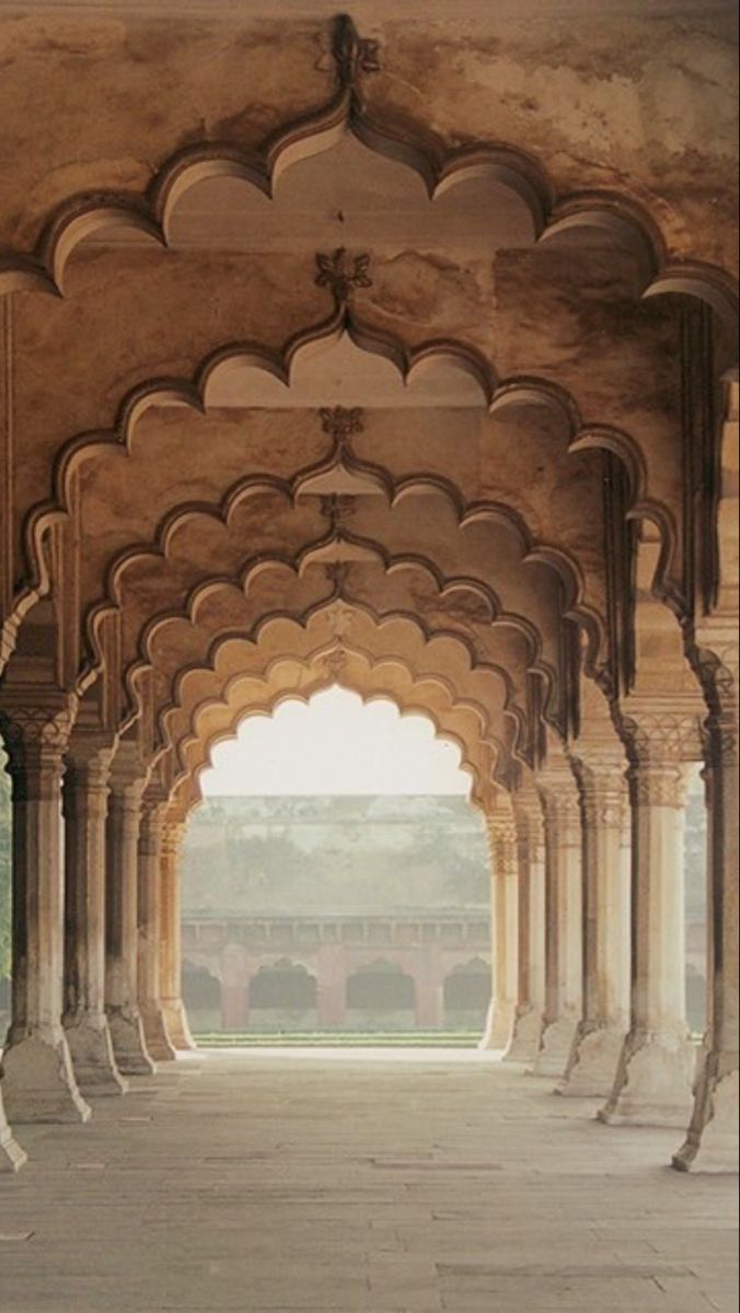 two giraffes are standing in an open area with arches and pillars on either side