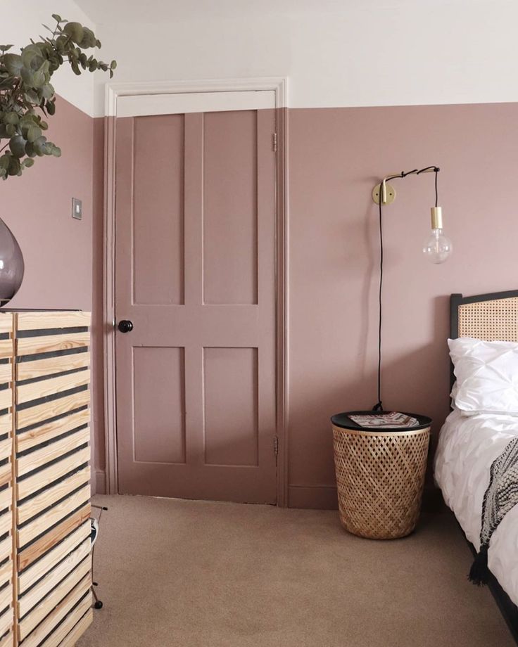 a bedroom with pink walls and white bedding, wicker basket next to the door