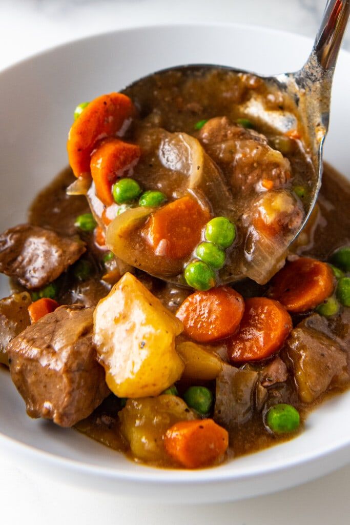 a white bowl filled with meat and vegetables on top of a table next to a fork