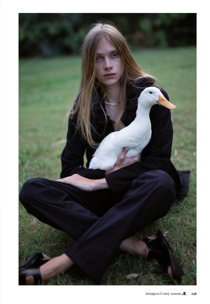 a woman sitting on the ground holding a white duck in her lap and looking at the camera