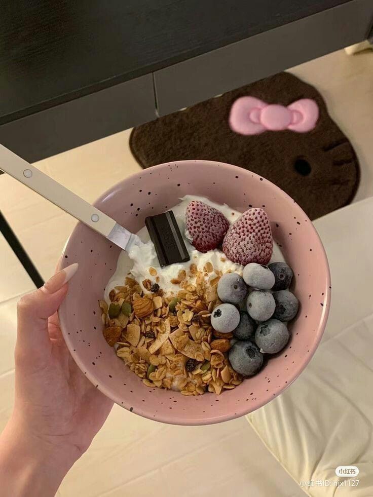 a person holding a pink bowl filled with yogurt, granola and berries