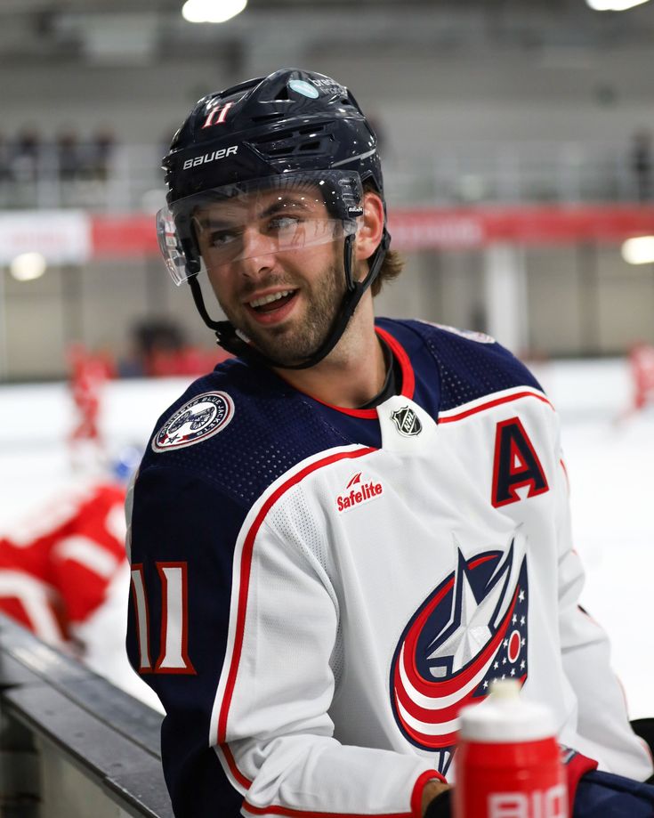 a hockey player sitting on the bench holding a cup in his hand and wearing a helmet