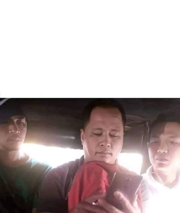 three men are looking at their cell phones in the back of a car while another man looks on