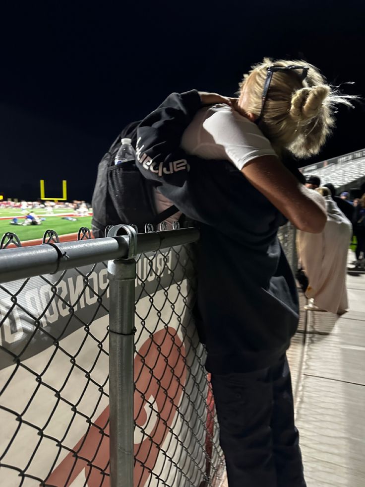 a woman leaning on a fence at a baseball game with her head over the fence