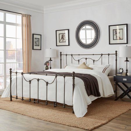 a bedroom with white walls and wood flooring has a metal bed frame in the middle