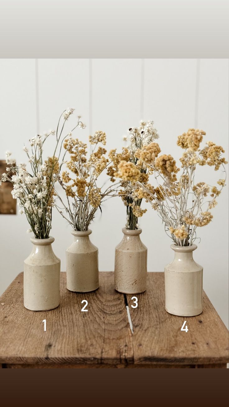 four vases with flowers in them sitting on a wooden table next to each other