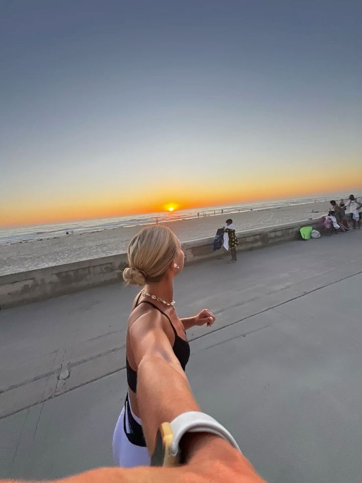 a woman is pointing at the sun setting over the ocean with people sitting on the beach in the background