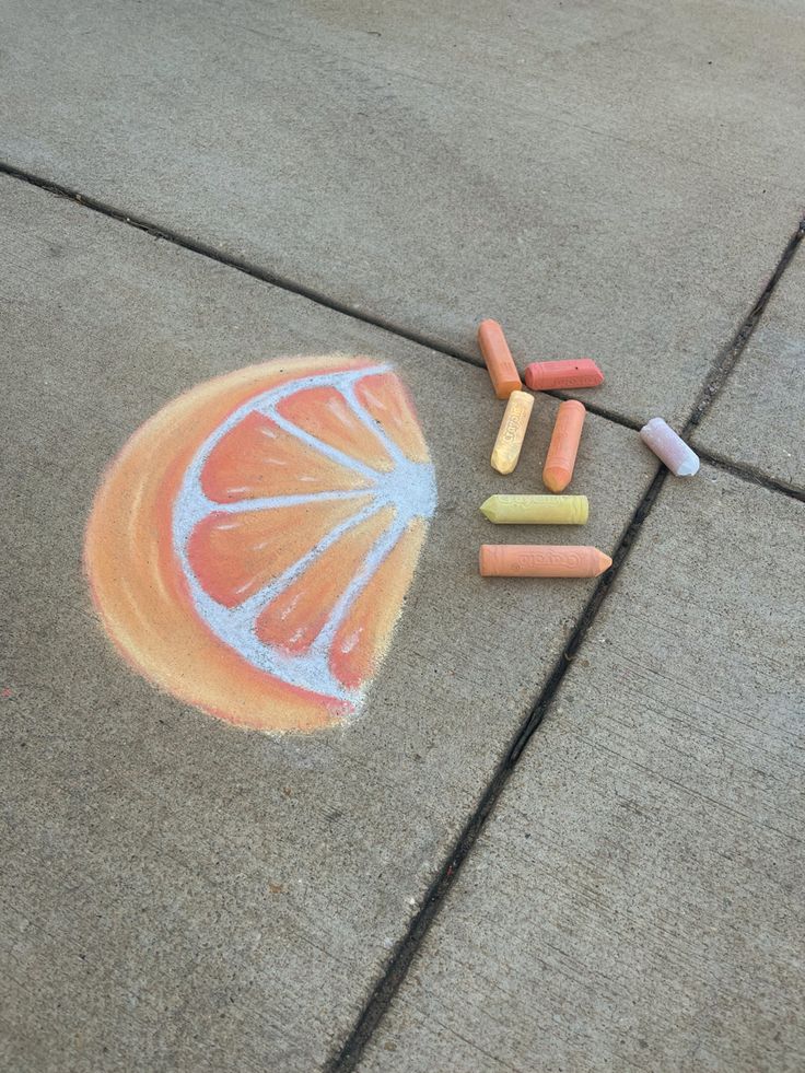 chalk crayons are laying on the sidewalk next to an orange slice and some crayons