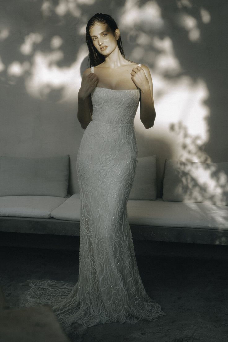 a woman standing in front of a couch wearing a white dress and posing for the camera