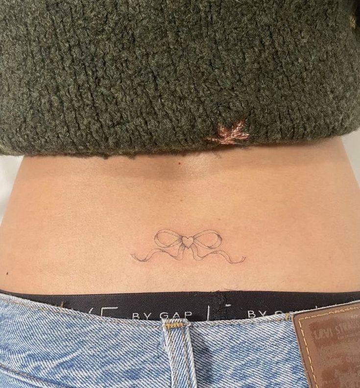 a woman's stomach with a bow tattoo on her lower back and the word love written in cursive writing