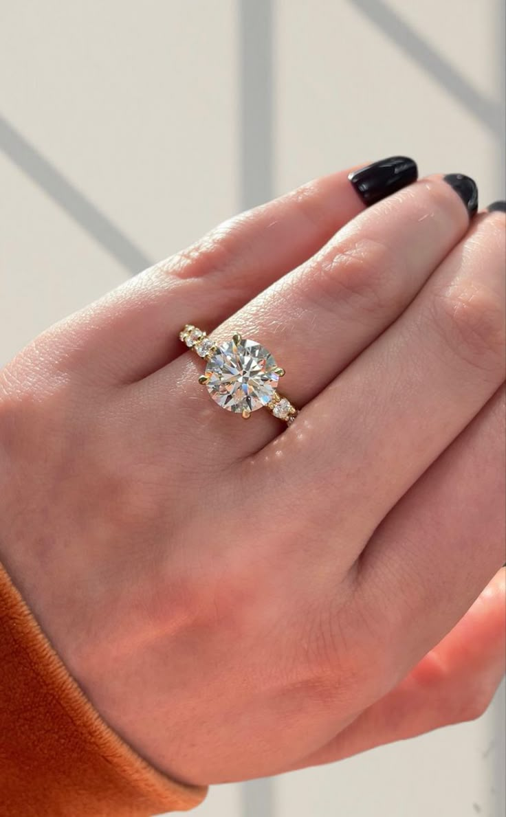 a woman's hand with a diamond ring on her left hand and an orange sweater