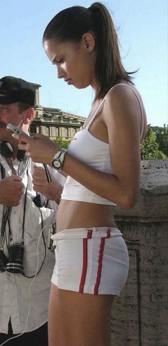 a woman in white shorts is looking at her cell phone while another man looks on