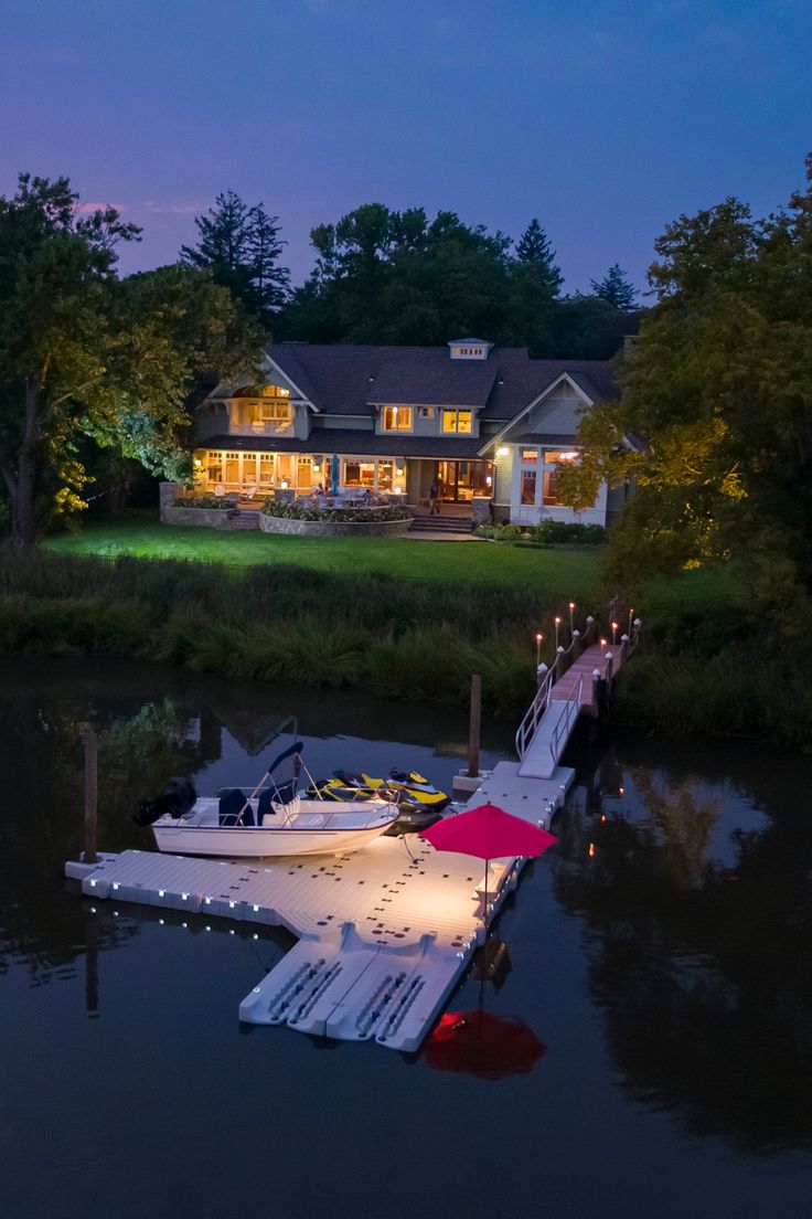 a boat is docked in the water near a house at night with lights on it