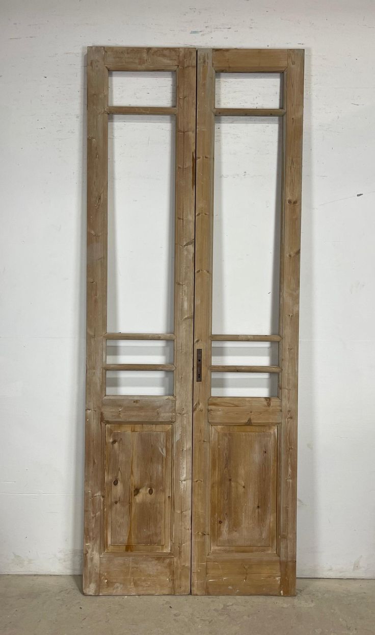 an old pair of wooden doors with glass panels on the top and bottom, against a white wall