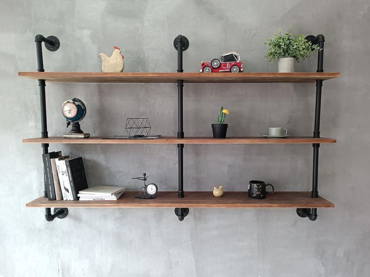 three wooden shelves with black pipe brackets and books on them, against a gray wall