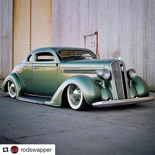 an old green car parked in front of a building