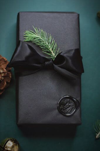 a present wrapped in black paper with a pine branch on it and a wax stamp