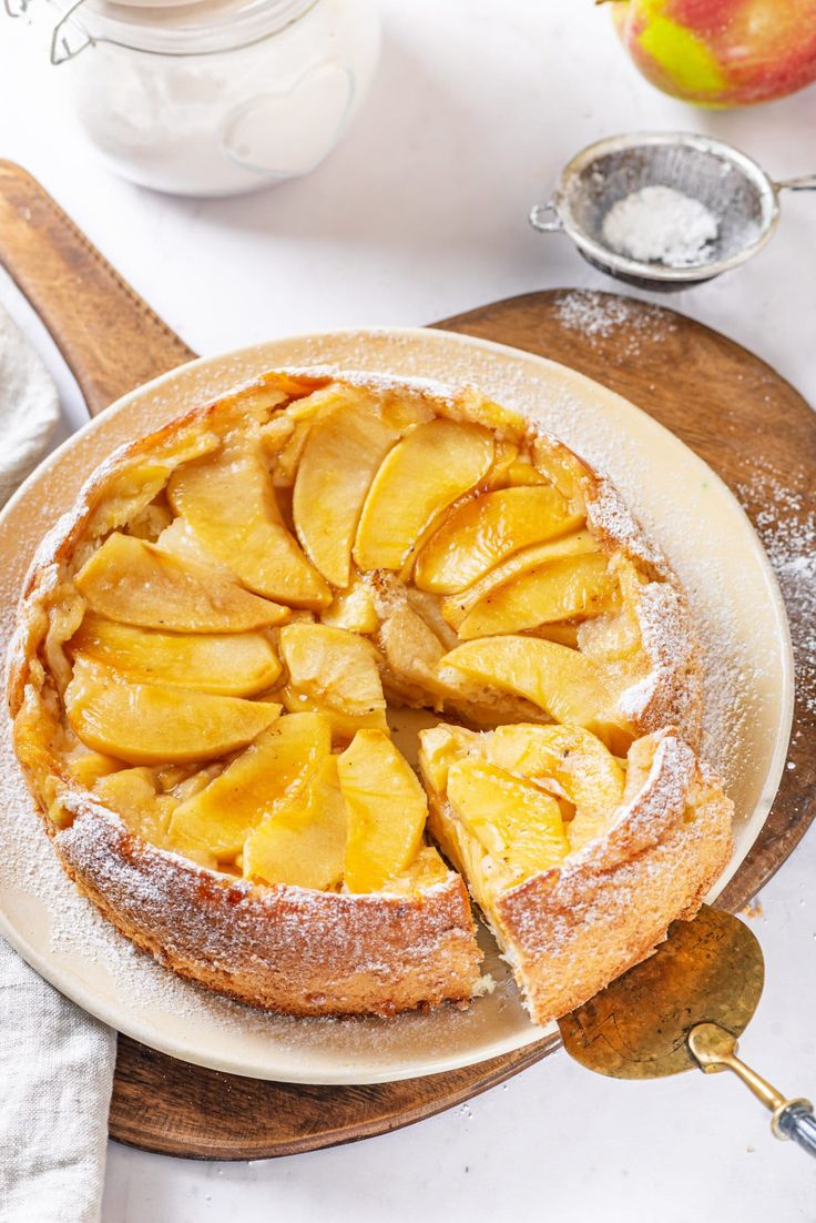 an apple pie is on a plate with powdered sugar and apples in the background