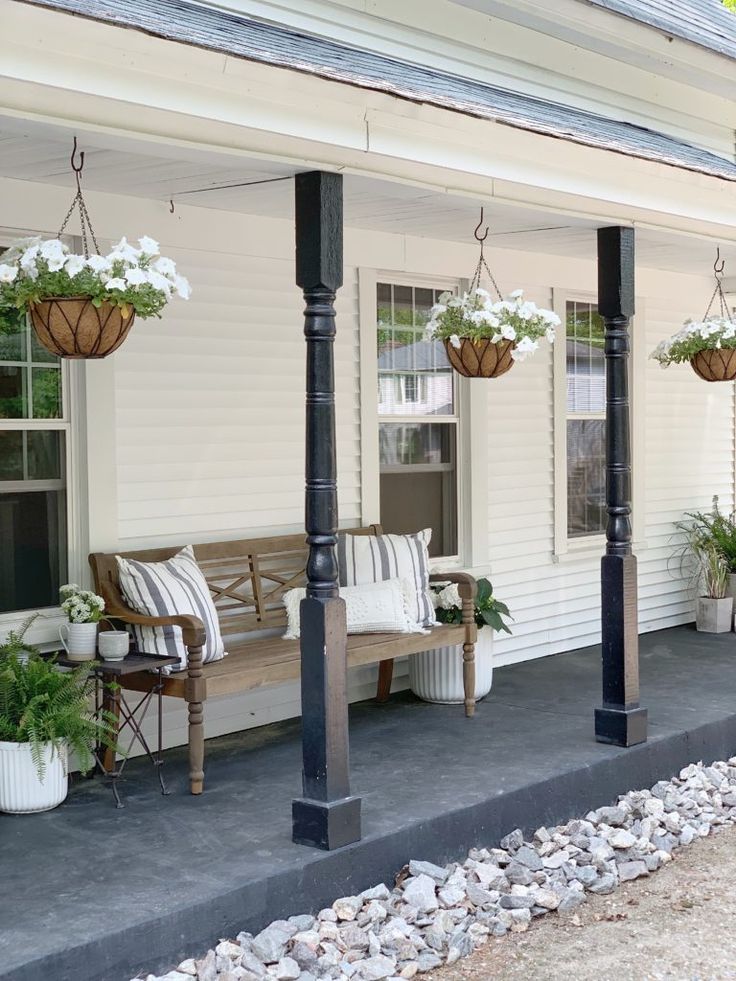 a porch with chairs and potted plants on the front steps, next to a white house