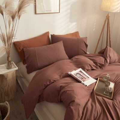 a bed with brown sheets and pillows in a white room next to a lamp on a table