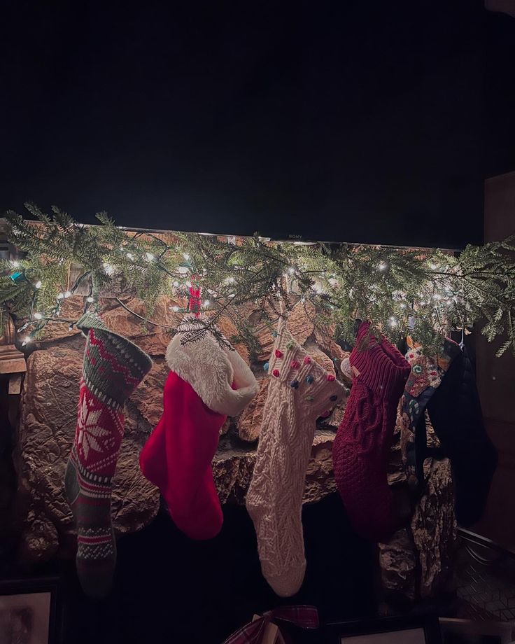 three stockings hanging from a christmas tree in front of a fireplace with lights on it