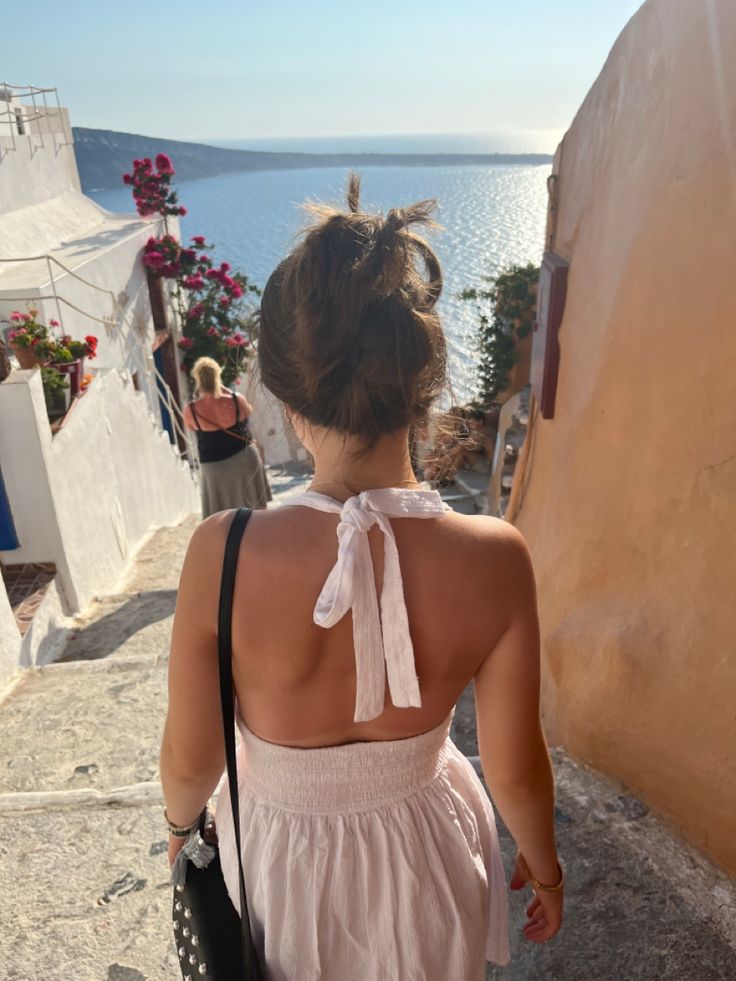 a woman in a pink dress is walking up the stairs to an ocean side building