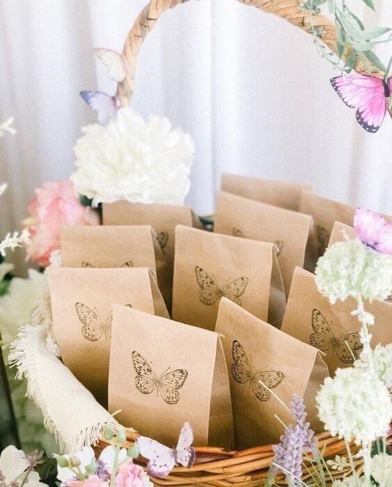 a basket filled with brown paper bags next to white flowers and butterflies on top of a table