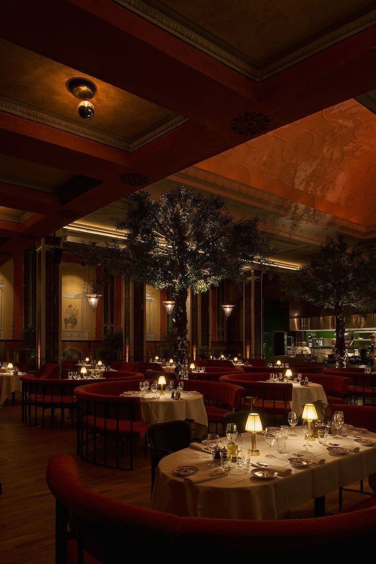 a dimly lit dining room with tables, chairs and trees in the center at night