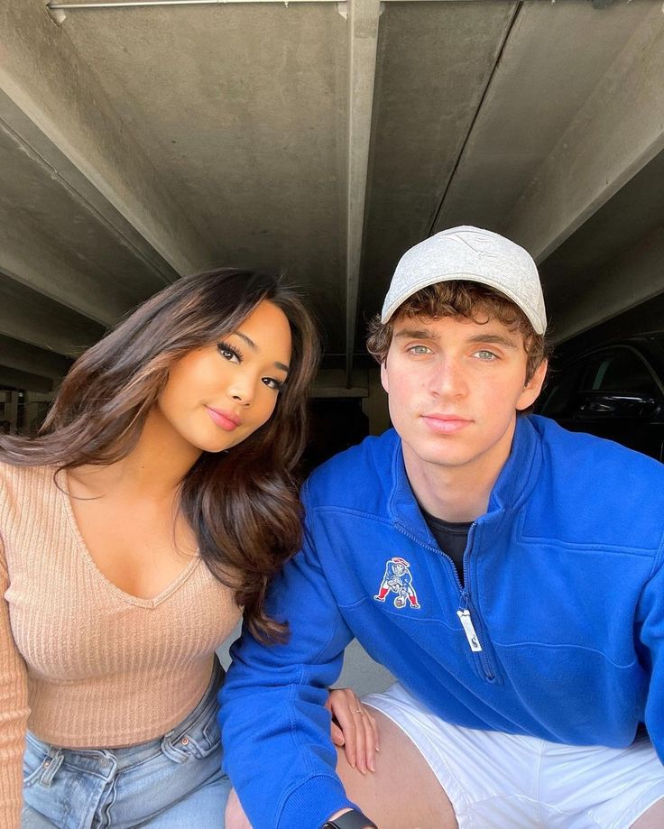 a young man and woman are sitting under a car