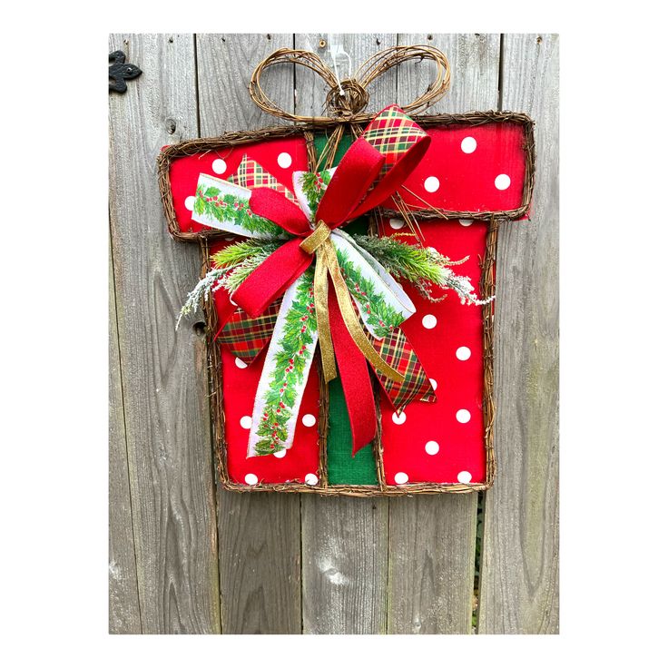 a red and green christmas present hanging on the side of a wooden fence with polka dots