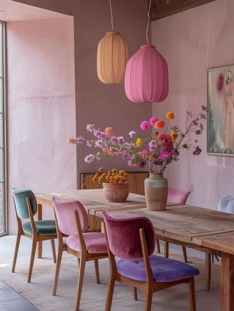 a dining room with pink walls and wooden table surrounded by colorful chairs, vases filled with flowers