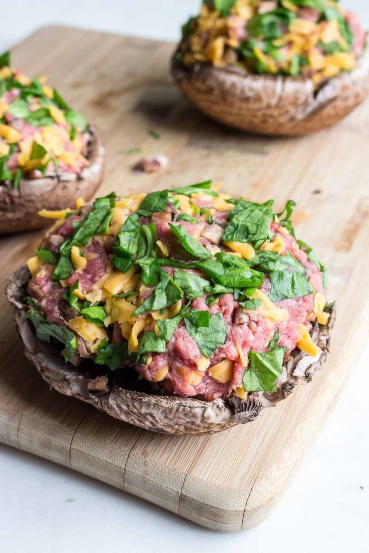 two stuffed mushrooms with cheese and spinach on a cutting board next to each other