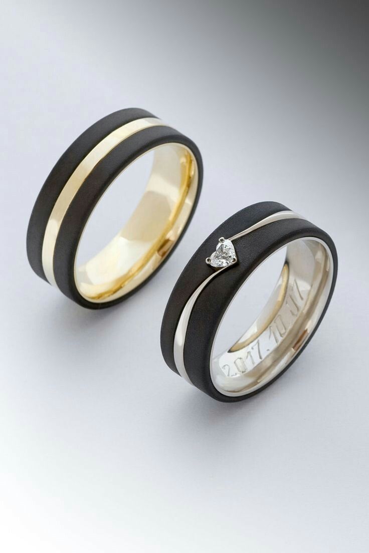 two wedding rings with black and gold bands, one has a diamond in the center