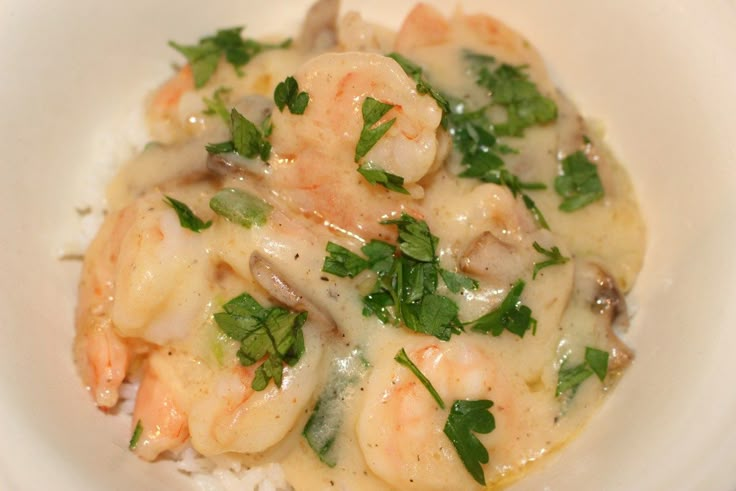 a white bowl filled with shrimp and rice covered in sauce, garnished with parsley