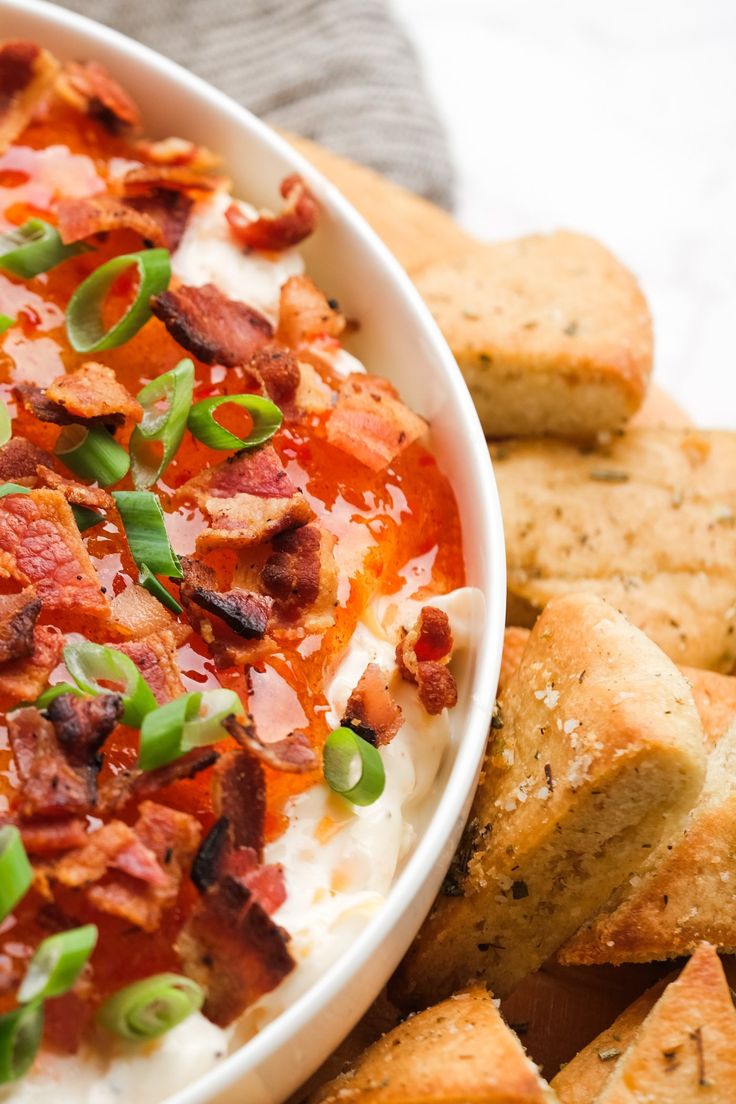 a white bowl filled with mashed potatoes covered in bacon and green onions next to crackers