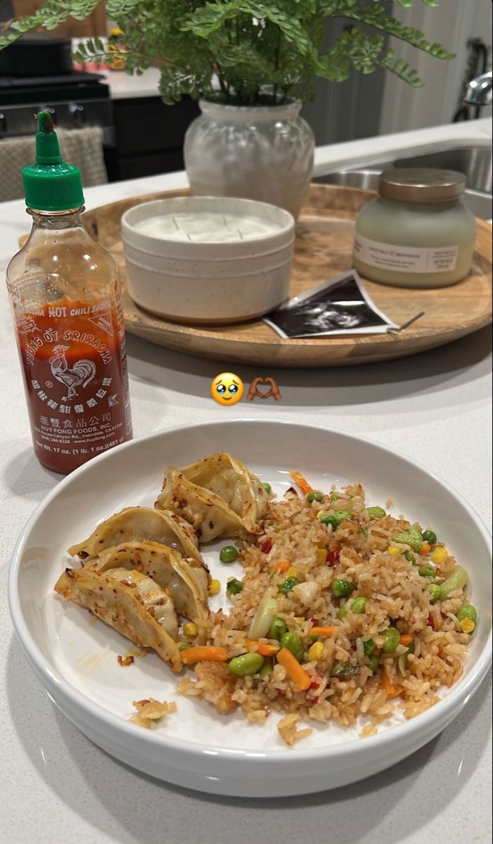 a white plate topped with rice and vegetables next to a bottle of sauce on a table