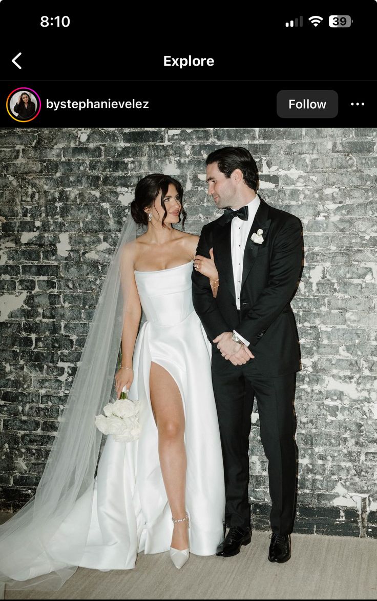 a bride and groom standing next to each other in front of a brick wall