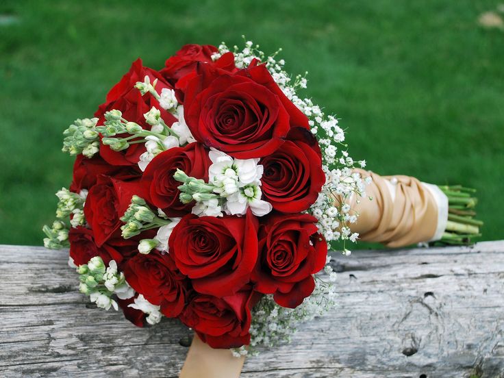 a bouquet of red roses and baby's breath sits on a piece of wood