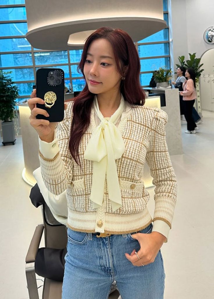 a woman taking a selfie with her cell phone in an office building while wearing jeans and a bow tie