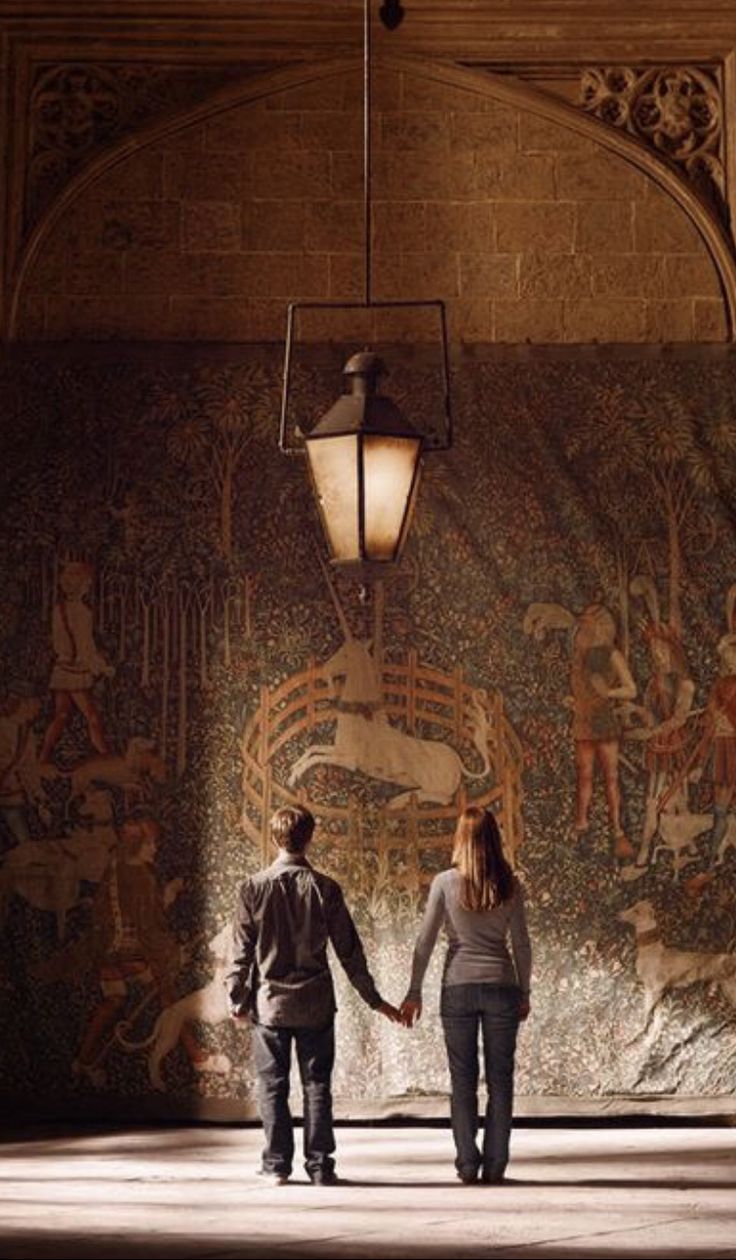 two people holding hands walking in front of a mural on the wall with lights above them