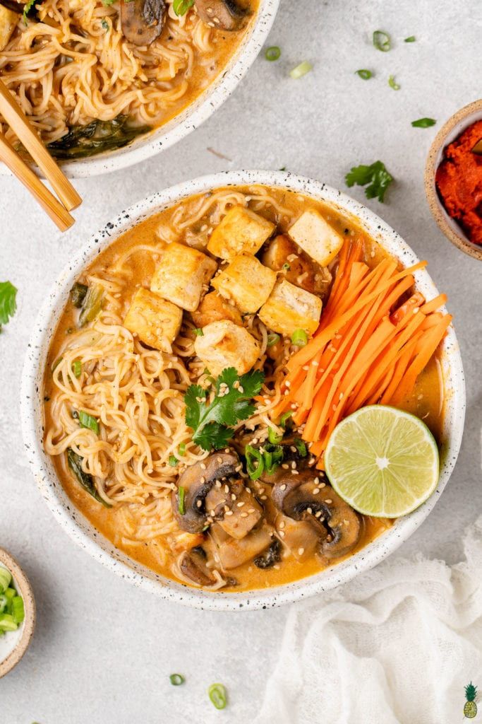 two bowls filled with noodles, tofu and carrots on top of a white table