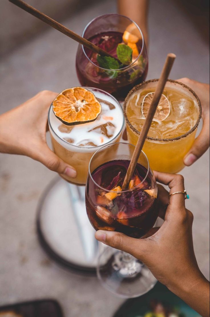 four people holding up glasses with drinks in them and orange slices on the rims