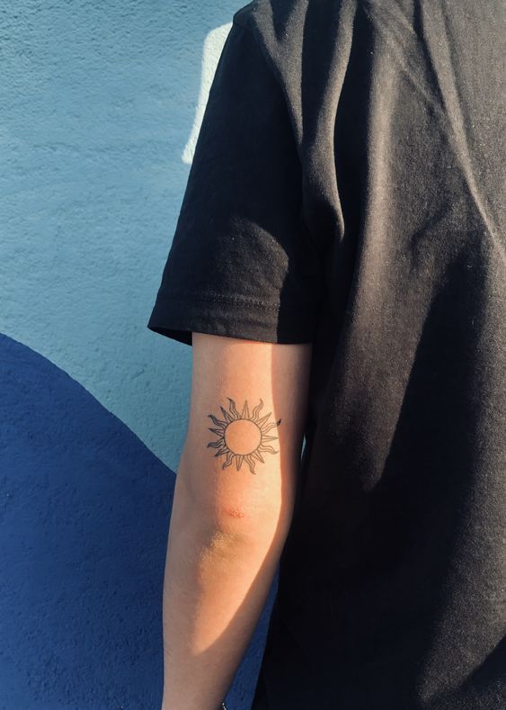 a person with a sun tattoo on their arm and back half is standing in front of a blue wall