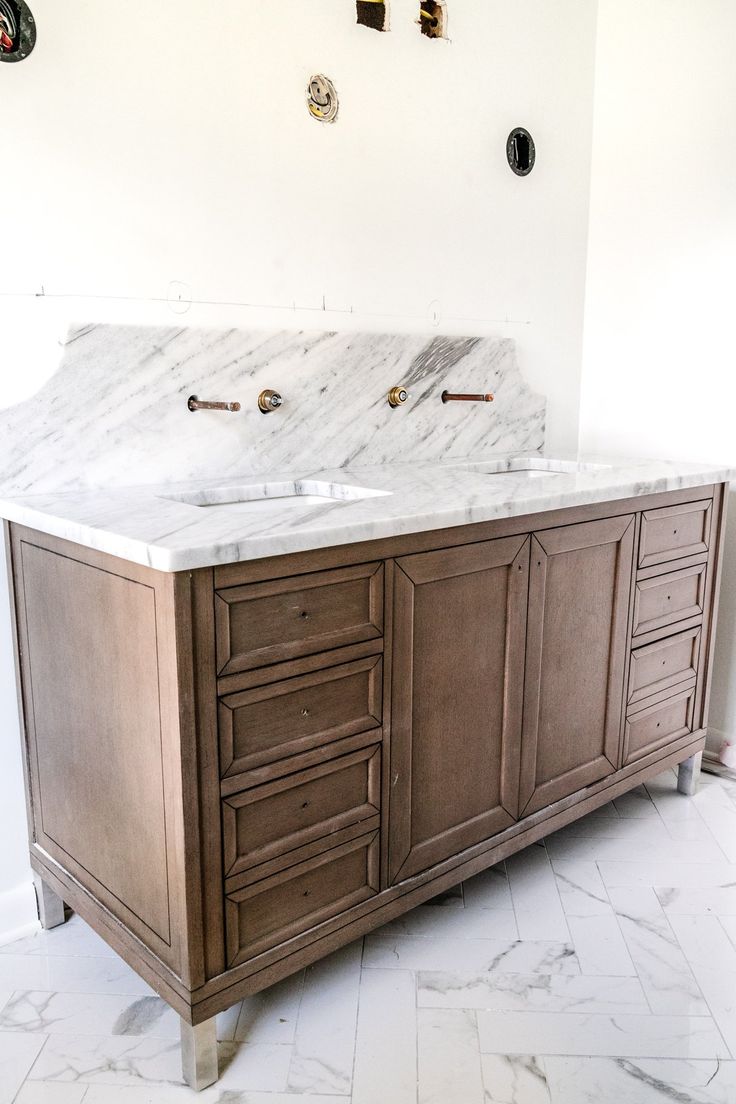 a bathroom vanity with two sinks and marble counter top in front of a white wall